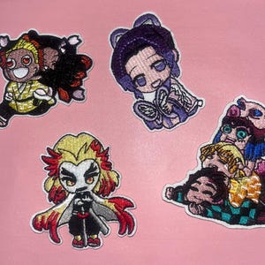 May include: Embroidered patches featuring anime characters in various poses. The patches showcase characters with distinctive hairstyles and outfits, including a character with a yellow and black outfit, and another with a purple kimono. The patches are on a pink background.