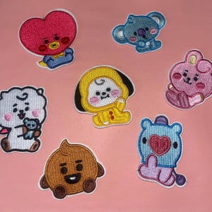 May include: A collection of embroidered patches featuring cartoon characters in various colors. The patches include a red heart-shaped character, a blue koala, a pink bunny, a white sheep, a yellow character, a brown character, and a blue character with a heart.