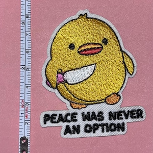 May include: Embroidered patch featuring a yellow chick holding a knife, with the text "PEACE WAS NEVER AN OPTION" in black letters on a white background. The patch is approximately 3 inches wide.