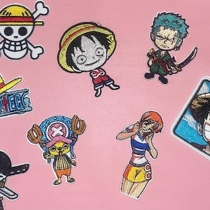 May include: A collection of embroidered patches featuring characters and symbols from the anime series One Piece. The patches include characters like Luffy, Zoro, and Chopper, along with the series logo and Jolly Roger.