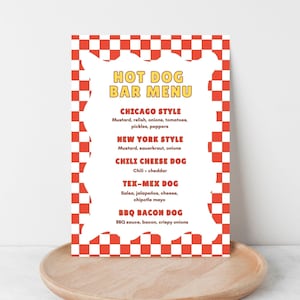 May include: A rectangular menu with a red and white checkered border. The menu features the text "HOT DOG BAR MENU" in yellow. Menu items include Chicago, New York, Chili Cheese, Tex-Mex, and BBQ Bacon hot dogs. The menu is on a wooden tray.