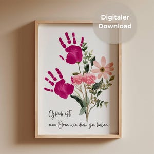 May include: A framed print with two magenta handprints and a watercolour floral arrangement. The artwork includes pink and peach flowers, green foliage, and the text "Digitaler Download" in a white circle.