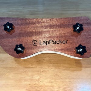 Puede incluir: Un escritorio de madera para port&aacute;til con un dise&ntilde;o curvo, con un acabado marr&oacute;n rojizo y cuatro perillas negras en forma de estrella. El escritorio tiene un borde curvo blanco y el texto "LapPacker" es visible.