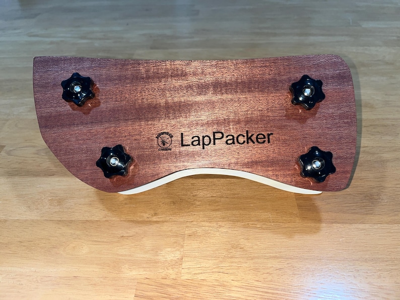 Puede incluir: Un escritorio de madera para port&aacute;til con un dise&ntilde;o curvo, con un acabado marr&oacute;n rojizo y cuatro perillas negras en forma de estrella. El escritorio tiene un borde curvo blanco y el texto "LapPacker" es visible.