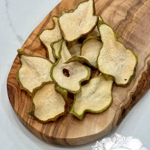 May include: Dried pear slices arranged on a wooden cutting board. The pear slices have a light tan color with green edges. The wooden board has a natural wood grain pattern. The image also includes a logo that says "Dried Harvest Co."