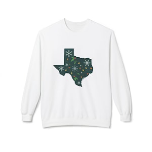 May include: White sweatshirt featuring a dark green Texas-shaped graphic filled with snowflakes, Christmas lights, and other festive elements. The long-sleeved top is perfect for holiday or seasonal wear.