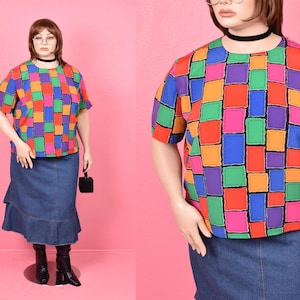 May include: A colorful, geometric patterned shirt with a short sleeve and a crew neck. The shirt is made of a lightweight fabric and has a relaxed fit. The shirt is paired with a denim skirt.