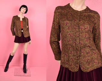 Könnte beinhalten: Vintage olivgrüne Jacke mit Paisley-Muster, kombiniert mit einem bordeauxfarbenen Faltenrock. Die Jacke hat einen runden Kragen und lange Ärmel. Die Schaufensterpuppe trägt schwarze Stiefel und eine goldfarbene Handtasche.