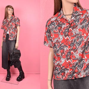 Puede incluir: Una camisa roja de manga corta con un estampado repetido de formas abstractas en blanco y negro. La camisa se combina con una falda vaquera y botas negras. Se sostiene una mochila negra en la mano.