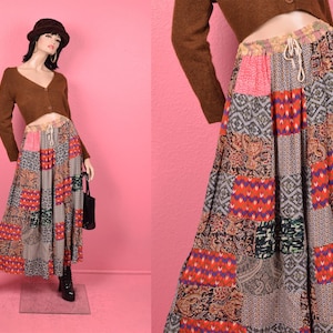 May include: A long, patchwork skirt with a drawstring waist. The skirt features a variety of patterned fabric squares in shades of red, orange, purple, green, and gray. The skirt is paired with a brown cropped cardigan.