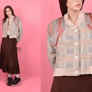 May include: A light blue and beige plaid cardigan with a button closure and pink ribbon accents. The cardigan has a knit texture and a relaxed fit.