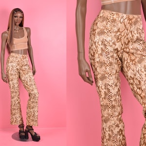 May include: A mannequin displays a snakeskin-patterned outfit against a pink backdrop. The ensemble includes high-waisted, flared pants and a matching crop top. The pants feature a brown and tan reptile print.