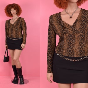 May include: A brown and black snake print long-sleeved shirt with a deep V-neckline. The shirt is paired with a black mini skirt and a silver chain belt.