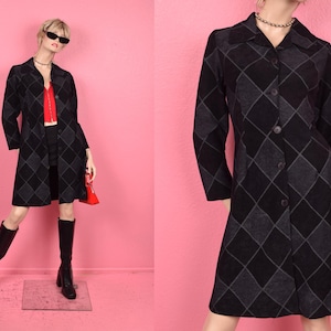 May include: A black and grey argyle pattern coat with a collared neckline and button-down front. The coat is knee-length and worn with black boots and a red top. A red purse is held in the hand.