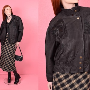 May include: Black leather jacket with a zipper closure and a textured design. The jacket has a stand-up collar and a  zippered pocket on the left sleeve.