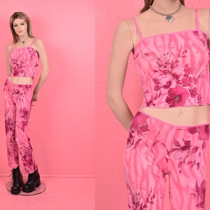 May include: A pink floral print two-piece outfit with a crop top and pants. The top has thin straps and a straight neckline. The pants have a straight leg.