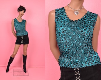 May include: A teal sleeveless top with a textured, bubble-like design. The top has a V-neck and is paired with a black mini skirt and knee-high black boots. A silver necklace with a heart pendant is also visible.