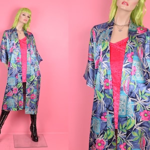 Könnte beinhalten: Eine blaue Satinrobe mit einem Blumendruck in Rosa-, Grün- und Weißtönen. Die Robe hat eine lange, fließende Silhouette und einen weiten, offenen Kragen.