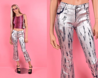 May include: Silver metallic flared jeans with a black and white abstract print. The jeans have a high waist and a slim fit through the legs.