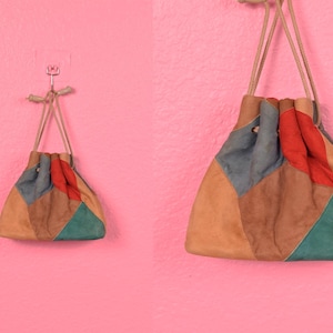 May include: Two patchwork drawstring bags made of suede in different colors. The larger bag is brown, blue, red, and green. The smaller bag is brown, green, and red.