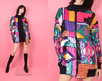 May include: A colorful sequined jacket with a geometric pattern in shades of pink, purple, green, and yellow. The jacket has a black collar, cuffs, and zipper. The jacket is worn over a black dress and paired with black boots.