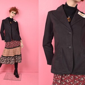 May include: A dark brown blazer with two buttons, worn over a black turtleneck and a floral print skirt. The skirt has a tiered design with red, tan, and black floral patterns. The mannequin is wearing black boots.