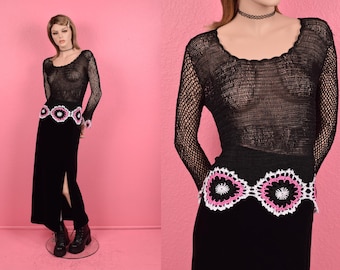 May include: Black crochet top with long sleeves and a pink and white crocheted belt. The top is sheer and has a loose fit.