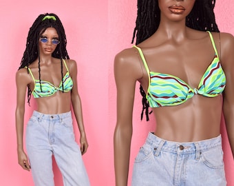 Puede incluir: Un top de bikini a rayas verdes, azules y marrones con cierre de nudo en la parte delantera. El top de bikini está en un maniquí con largas rastas negras y pantalones vaqueros azules.