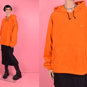 May include: A bright orange fleece hoodie with a drawstring hood and a kangaroo pocket. The hoodie has a small logo on the front.