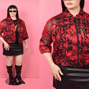 May include: A red and black floral patterned jacket with a zipper closure. The jacket has three-quarter sleeves and is paired with a black skirt and boots. The mannequin is wearing sunglasses.