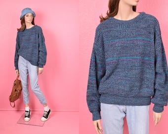 May include: A blue knit sweater with horizontal stripes of teal and purple. The sweater is displayed on a mannequin, paired with light blue jeans, a matching blue bucket hat, and black and white sneakers. A brown backpack is also included.