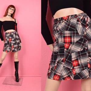 May include: A black and red plaid mini skirt with a silver chain belt. The skirt is made of a patchwork of different plaid fabrics.