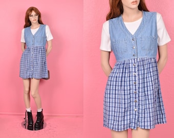 May include: A vintage denim vest dress. The dress features a blue and white plaid skirt with a button-down front and a denim vest top. The model is wearing a white t-shirt underneath the vest. The dress is paired with black boots.