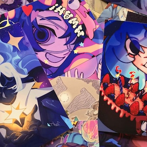 May include: A collection of colorful art prints featuring anime-style characters. The prints showcase vibrant colors, including blues, purples, and pinks. Some prints have text, and others depict fantasy themes, including a birthday cake and a character labeled "Thief."