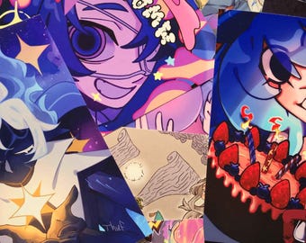 May include: A collection of rectangular art prints featuring vibrant, stylised anime-inspired illustrations. The prints display diverse characters, a strawberry-topped cake with lit candles, and cosmic themes in shades of blue, pink, and purple.