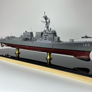May include: A detailed model warship in grey with a red hull, mounted on a black base with gold supports. The ship features intricate details, including radar and weaponry, and the number 125 is visible on the bow.