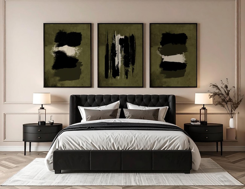 May include: Three framed abstract art prints with black, white, and olive green brushstrokes hang above a bed. The bed has a black headboard, white bedding, and two black nightstands with lamps. A rug is on the floor.