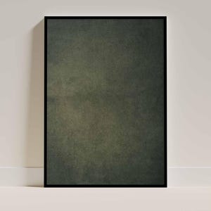 May include: A framed art print featuring a textured, dark green abstract design. The artwork is enclosed in a black frame and leans against a white wall and baseboard.