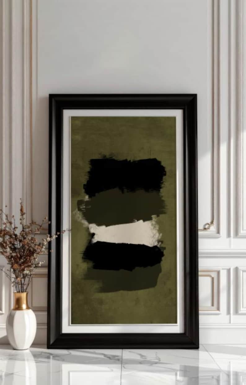 May include: Abstract art print in a black frame. The artwork features horizontal brushstrokes in black, olive green, and white against an olive green background. A white vase with gold accents and dried flowers sits to the left.