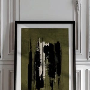 May include: Abstract art print in a black frame. The artwork features vertical brushstrokes in black and white against an olive green background. The framed art is displayed against a white wall.