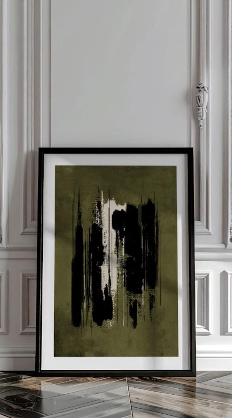 May include: Abstract art print in a black frame. The artwork features vertical brushstrokes in black and white against an olive green background. The framed art is displayed against a white wall.