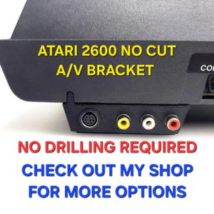 May include: A black A/V bracket for an Atari 2600 console featuring one circular multi-pin port and three RCA ports in yellow, white, and red. The text reads: ATARI 2600 NO CUT A/V BRACKET, NO DRILLING REQUIRED, CHECK OUT MY SHOP FOR MORE OPTIONS.