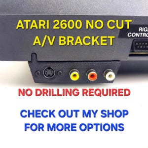 Puede incluir: Un soporte A/V negro impreso en 3D para consola Atari 2600, con un puerto circular y tres conectores RCA en amarillo, rojo y blanco. El texto dice: ATARI 2600 NO CUT A/V BRACKET, NO DRILLING REQUIRED, CHECK OUT MY SHOP FOR MORE OPTIONS.