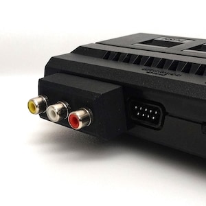 May include: A close-up of a black retro games console. It has yellow, white, and red RCA connectors, plus a 9-pin connector. The top has a vent and the word "PUSH".