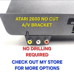Könnte beinhalten: Eine schwarze Kunststoffhalterung für Atari 2600 ohne Ausschnitt mit drei RCA-Anschlüssen in Gelb, Weiß und Rot. Der Text auf dem Bild lautet: ATARI 2600 NO CUT A/V BRACKET, NO DRILLING REQUIRED, CHECK OUT MY STORE FOR MORE OPTIONS.