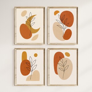Könnte beinhalten: Vier gerahmte Kunstdrucke mit abstrakten Designs. Jeder Druck hat einen beigen Hintergrund mit rost-, beige- und goldfarbenen Formen sowie eine schwarze Strichzeichnung einer Pflanze. Die Rahmen sind goldfarben.