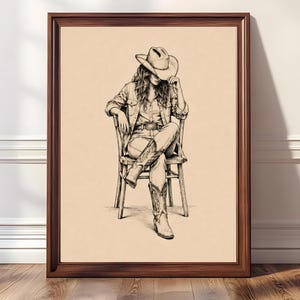 Puede incluir: Impresión artística en blanco y negro enmarcada de una persona con sombrero de vaquero, camisa vaquera y vaqueros, sentada en una silla de madera. La obra de arte presenta sombreado y líneas detalladas. El marco es de color marrón oscuro.