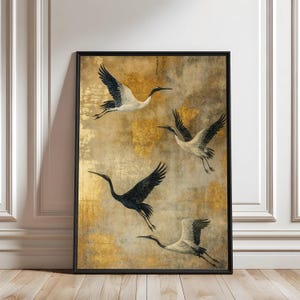 Puede incluir: Una impresión de arte mural enmarcada que muestra cuatro grullas volando en blanco y negro sobre un fondo texturizado y moteado de tonos oro metálico y beige apagado. Las aves se representan en varias posiciones de vuelo con cuellos largos.