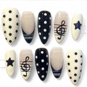 May include: A set of ten artificial nails in various designs. Some nails are off-white with black polka dots, others are black with white polka dots. Two nails feature a black treble clef design, and two have a black star. The remaining nails have a black and white striped design.