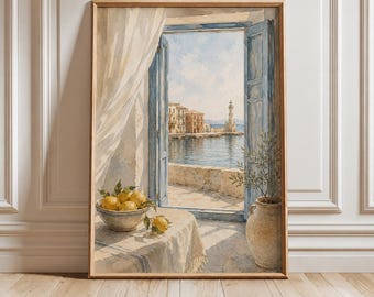 May include: A framed watercolor painting depicting an open window with blue shutters overlooking a coastal town and lighthouse. A bowl of yellow lemons sits on a table covered by a white cloth, next to a tall ceramic vase with a small green plant.